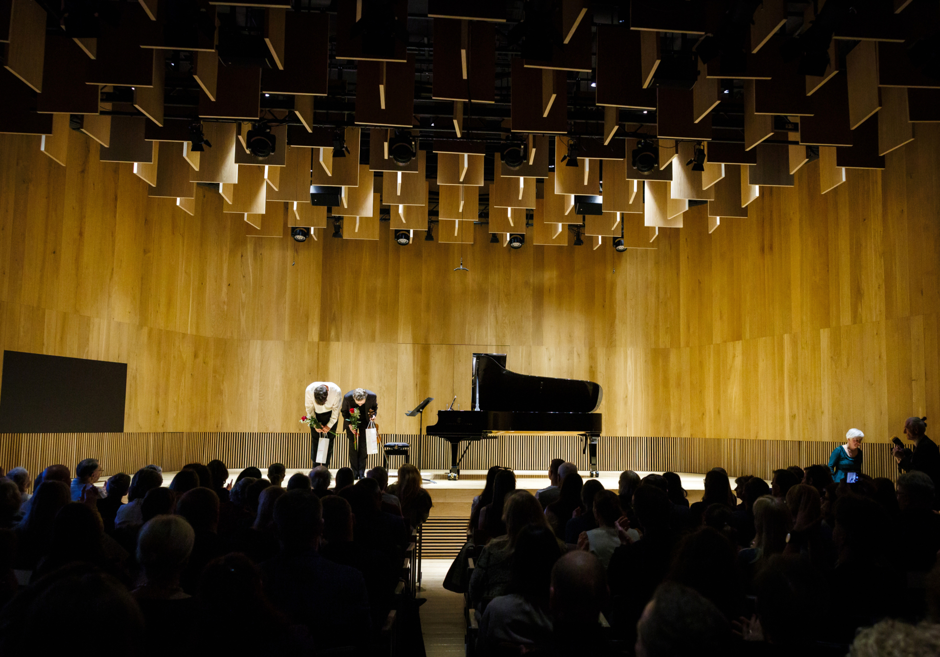 violinist and pianist on stage, crowd of vievers in audience