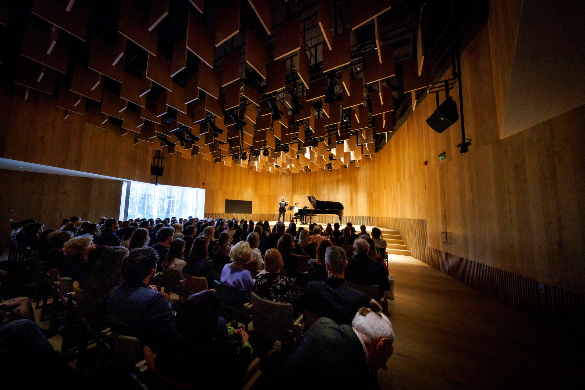 violinist and pianist on stage, crowd of vievers in audience