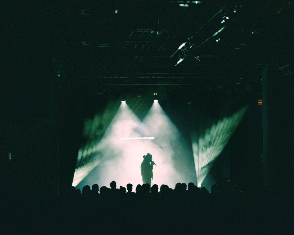an artist on stage in the lights in front of gahtered audiences